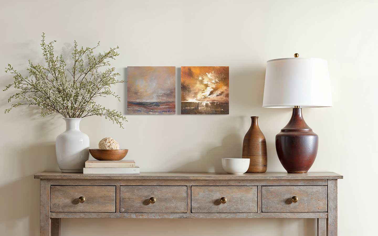 Wooden console table with decorative items against a wall with two pieces of abstract art.